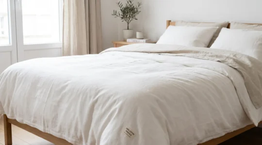 Lit habillé d'une housse de couette en percale de coton blanche dans une chambre lumineuse aux tons naturels, texture du tissage visible au premier plan